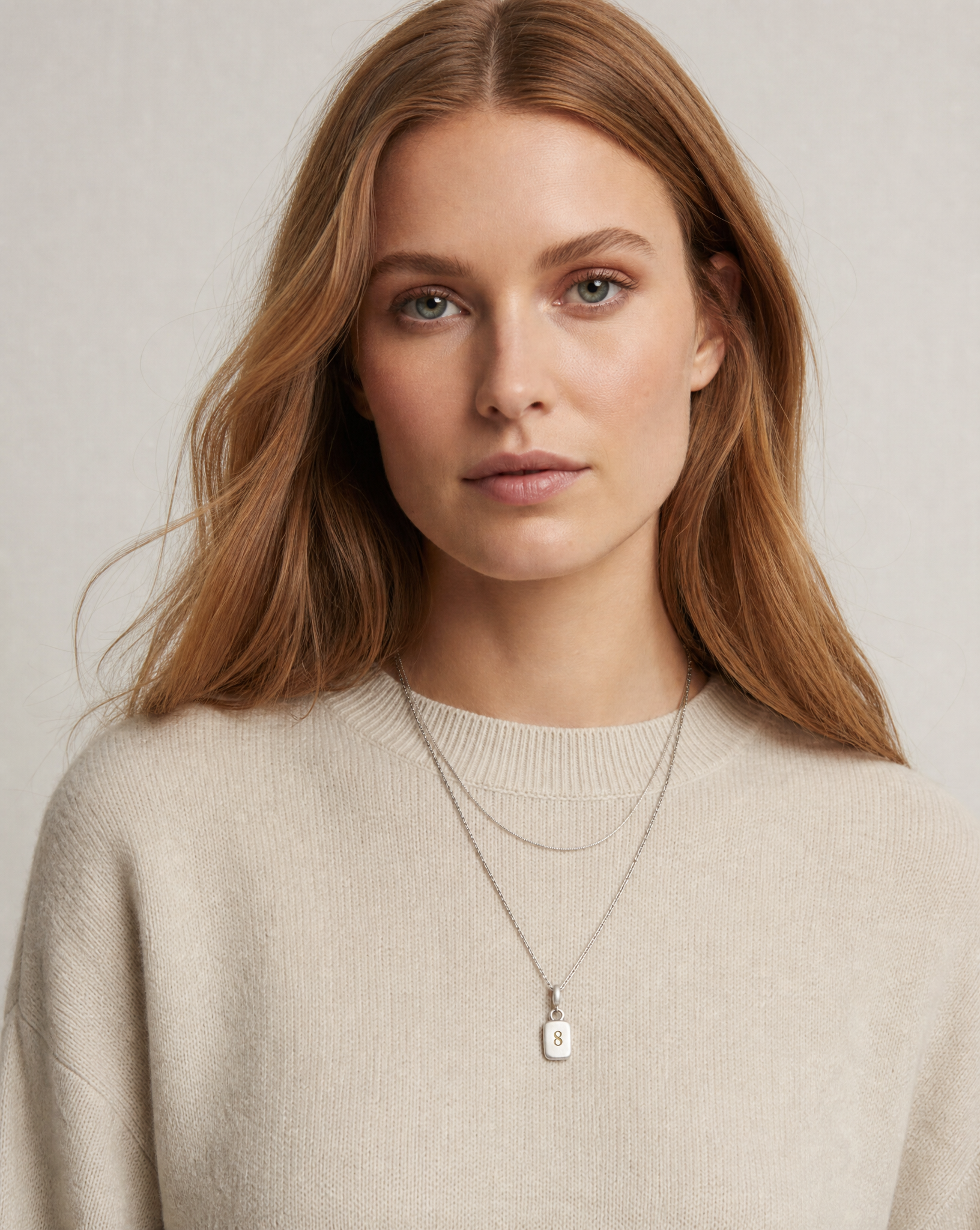 Golden Horn Number 8 pendant layered with a thin silver chain over a cream knit jumper