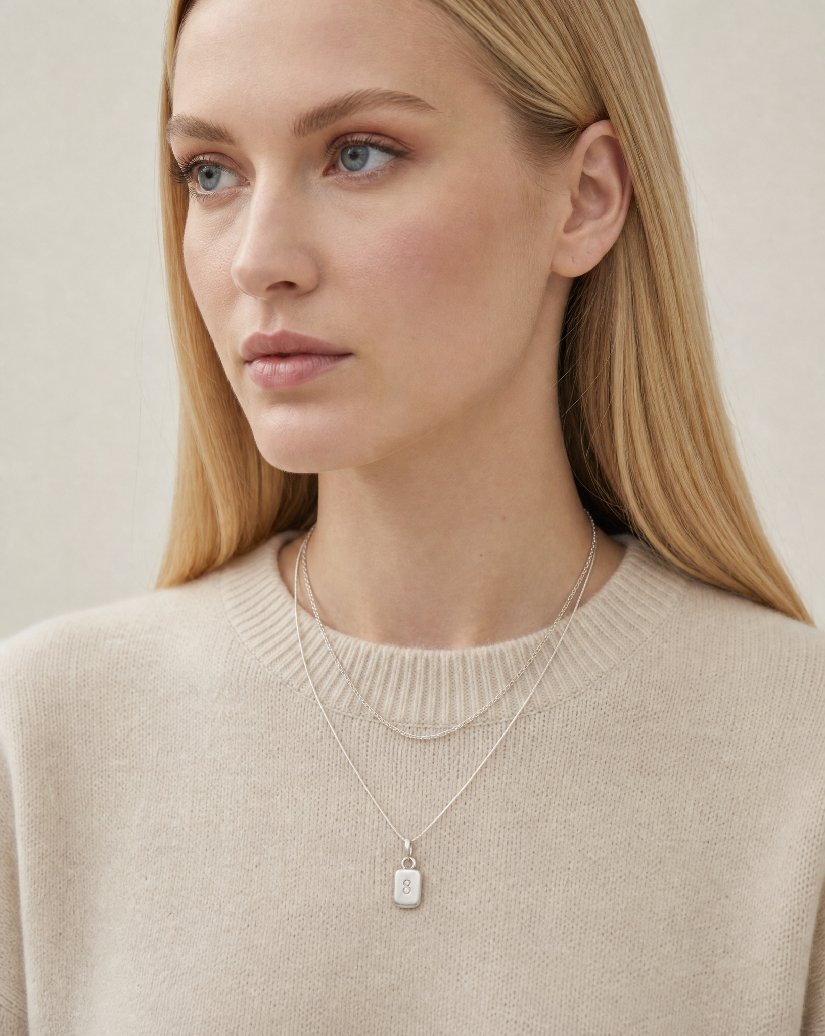 Layered sterling silver necklaces with Number 8 pendant, close-up over a cream knit jumper