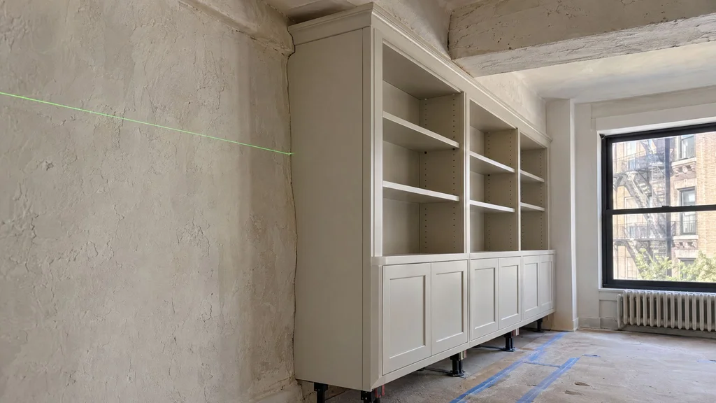 Painted bookcase end panel scribed tight to an uneven plaster wall and beam during installation in a pre-war New York apartment