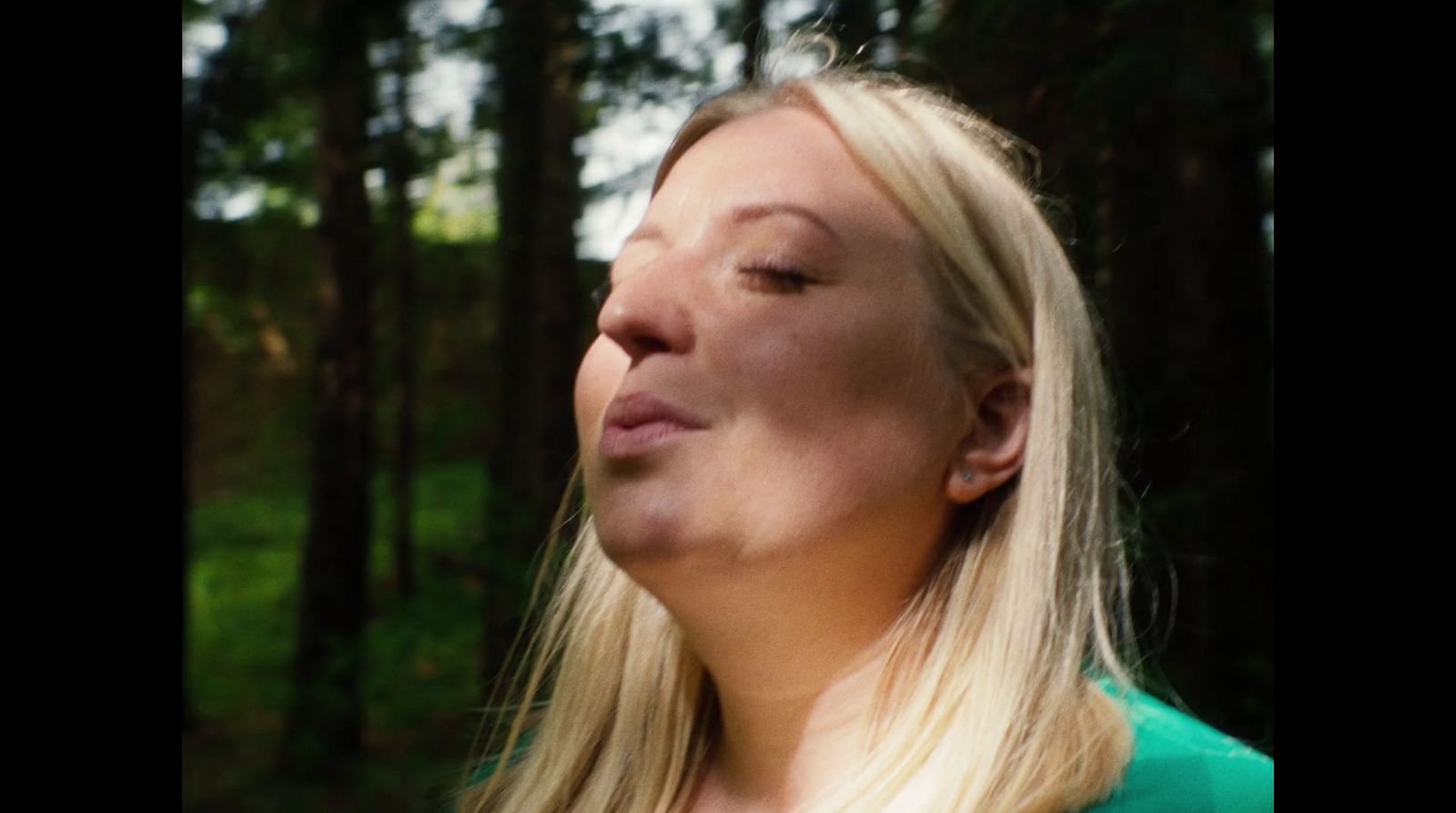 a woman with long blonde hair standing in a forest