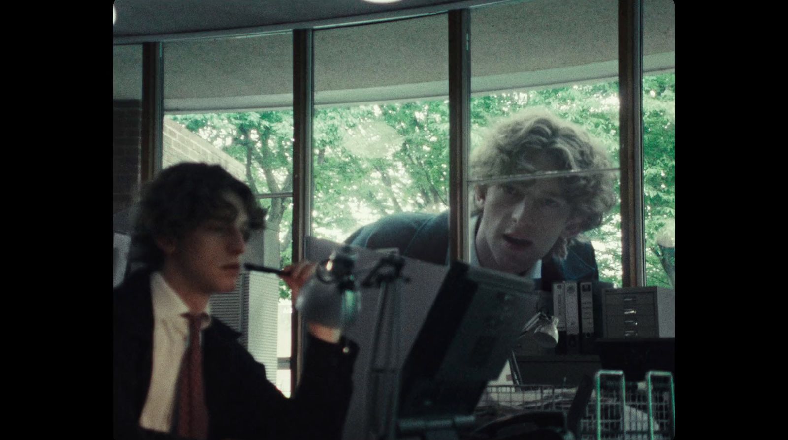 a man in a suit and tie smoking a cigarette in front of a computer monitor