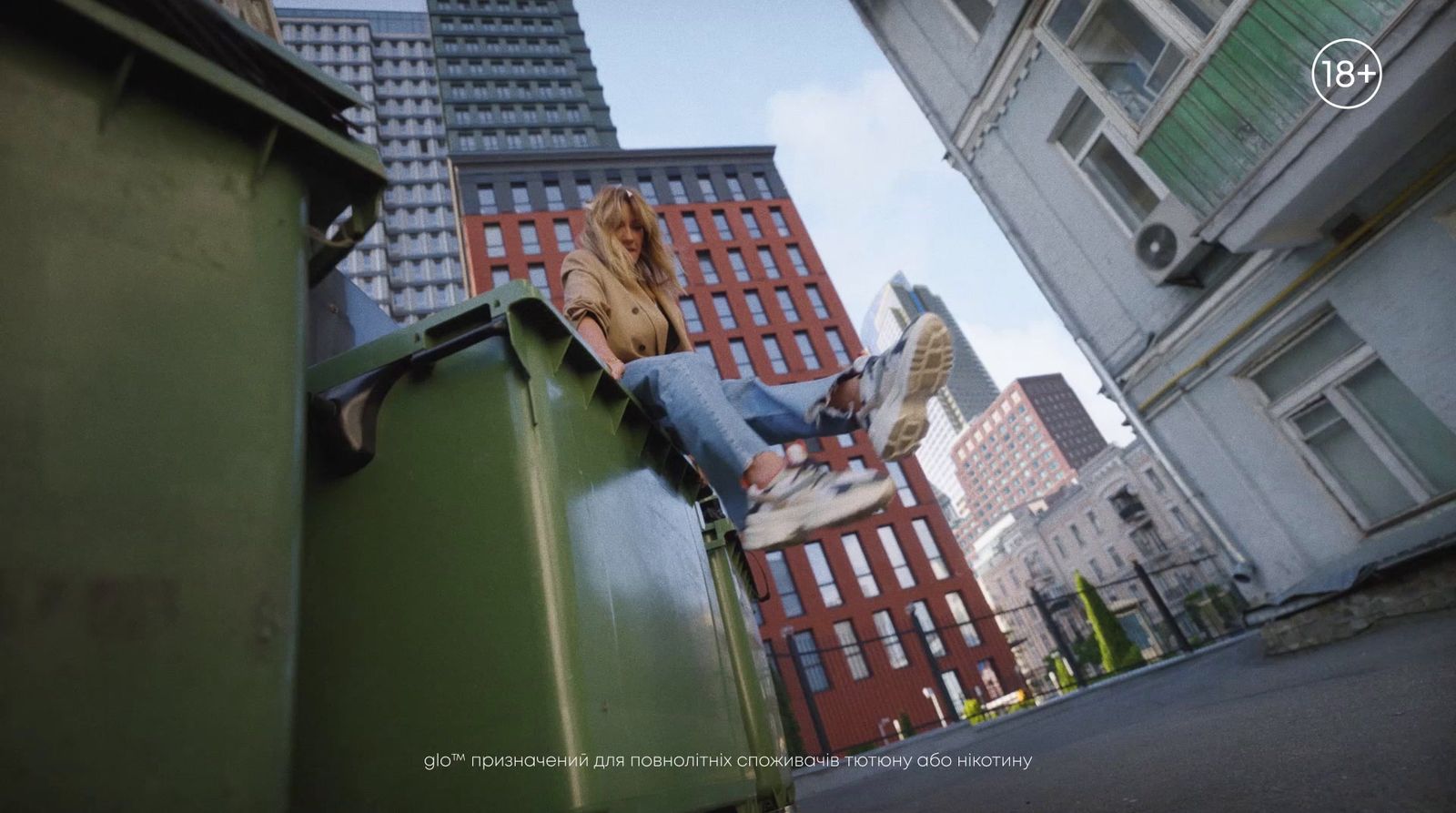 a woman sitting on top of a green trash can