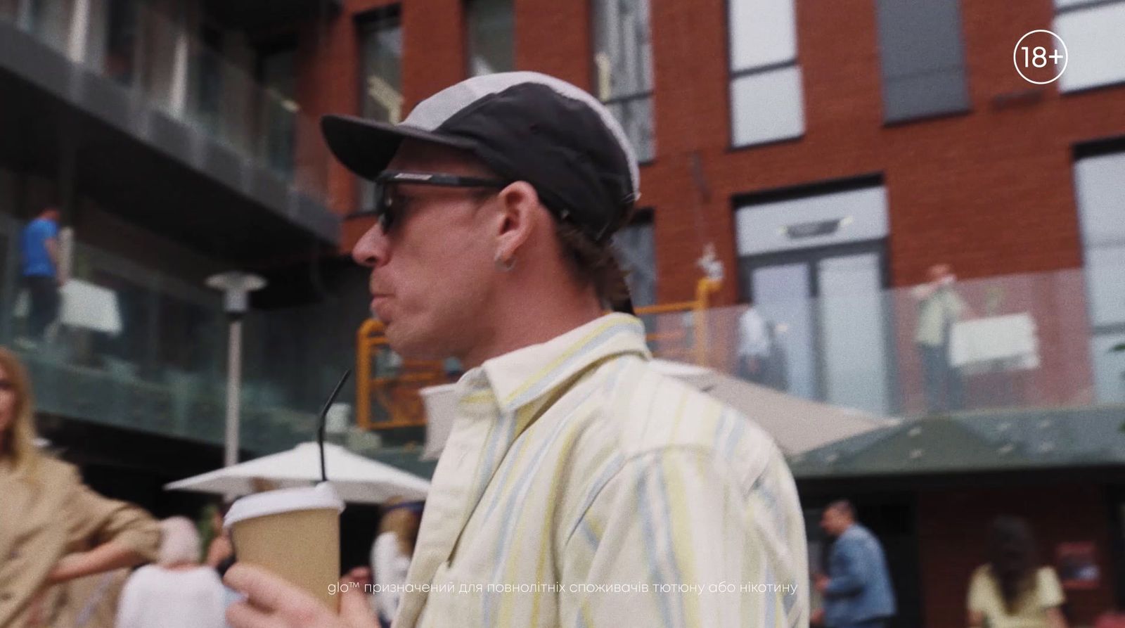 a man in a hat and sunglasses holding a cup of coffee