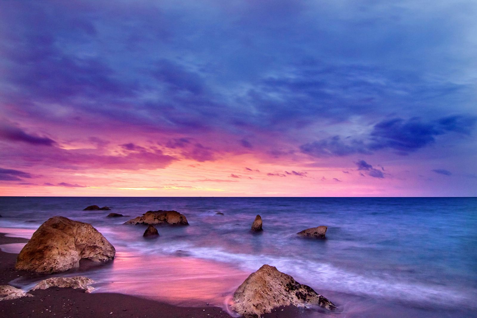 a beautiful sunset over the ocean with rocks in the foreground