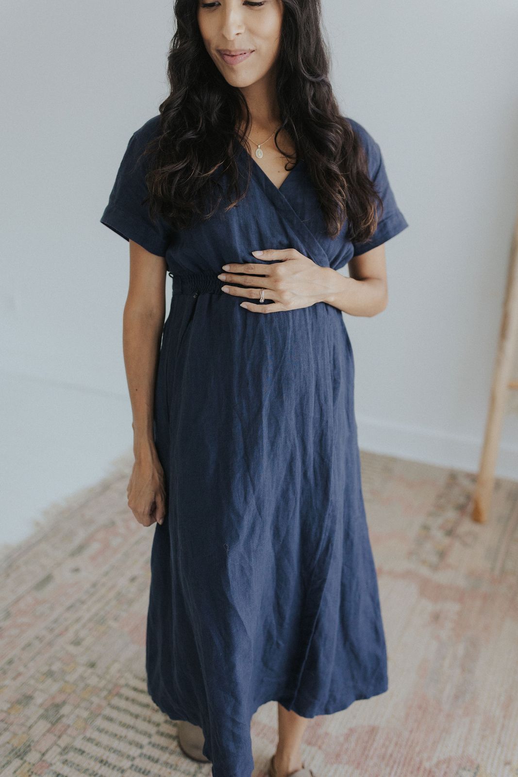a pregnant woman in a blue dress standing on a rug