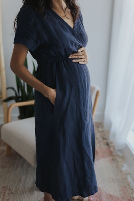 a pregnant woman in a blue dress standing in front of a window