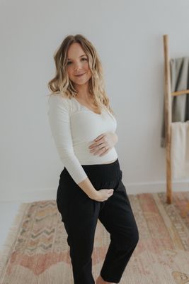 a pregnant woman standing in a white top and black pants