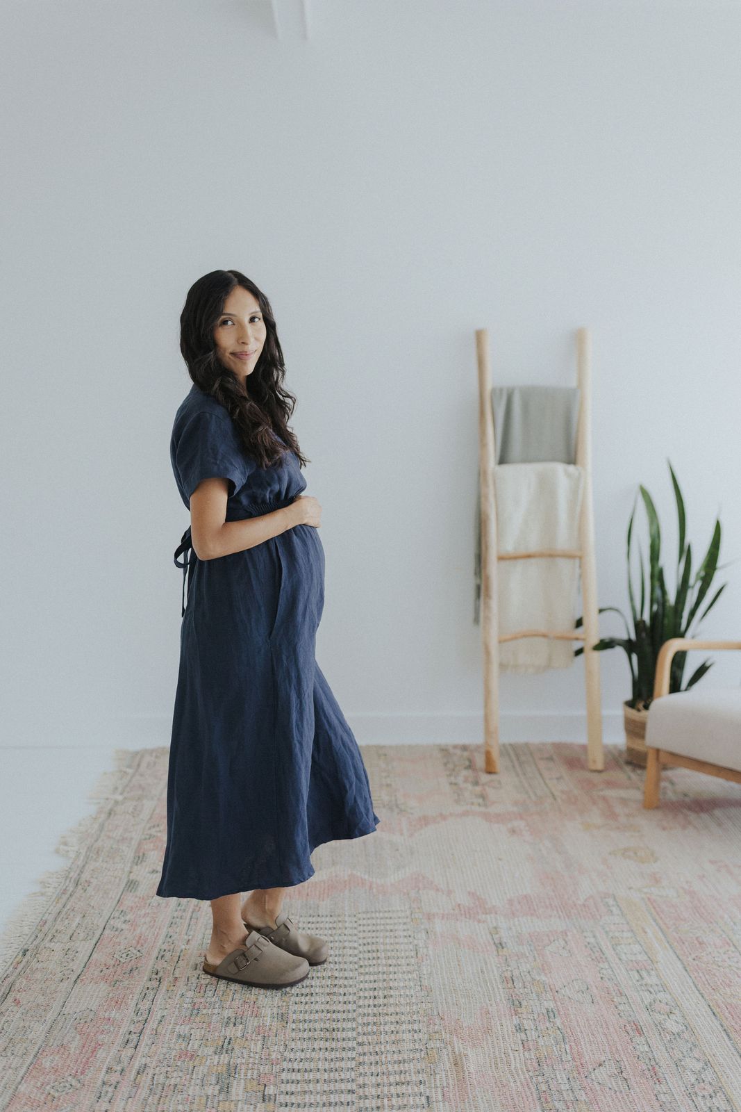 a pregnant woman standing on a rug in a white room