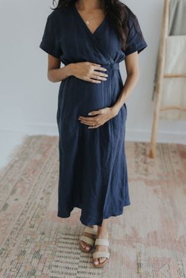 a pregnant woman in a blue dress standing on a rug