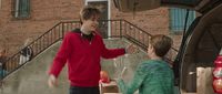 a boy handing something to another boy in front of a car