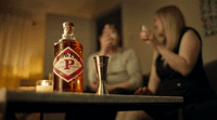 two women sitting at a table with a bottle of liquor