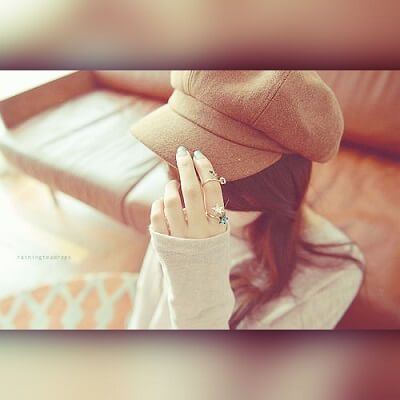 a woman wearing a hat and holding her hand up to her face