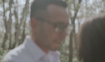 a man wearing glasses standing in front of a forest