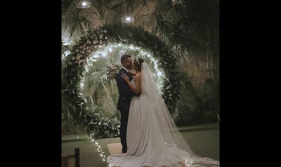 a bride and groom kissing in front of a floral arch