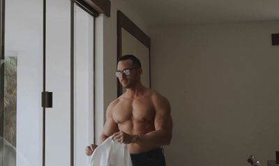 a shirtless man holding a white bag in his hand