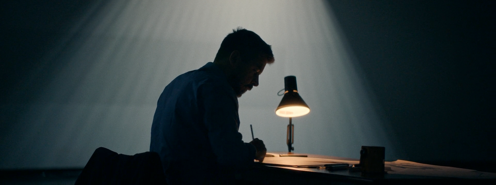 a man sitting in front of a desk with a lamp on it