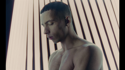 a shirtless man standing in front of a striped wall