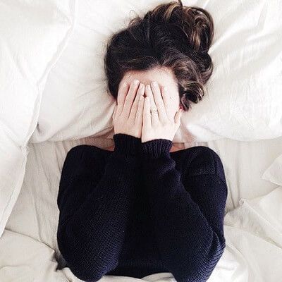 a woman laying in bed covering her face with her hands