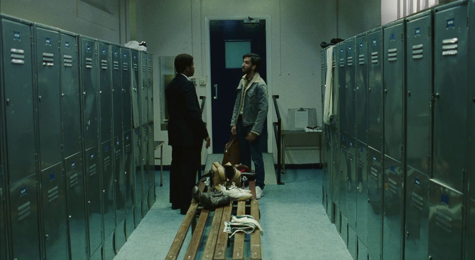 a couple of men standing in a hallway next to lockers