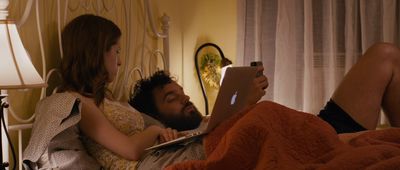 a man and a woman laying in bed looking at a tablet