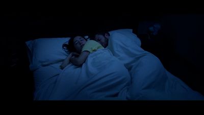 a man and a woman laying in bed in the dark