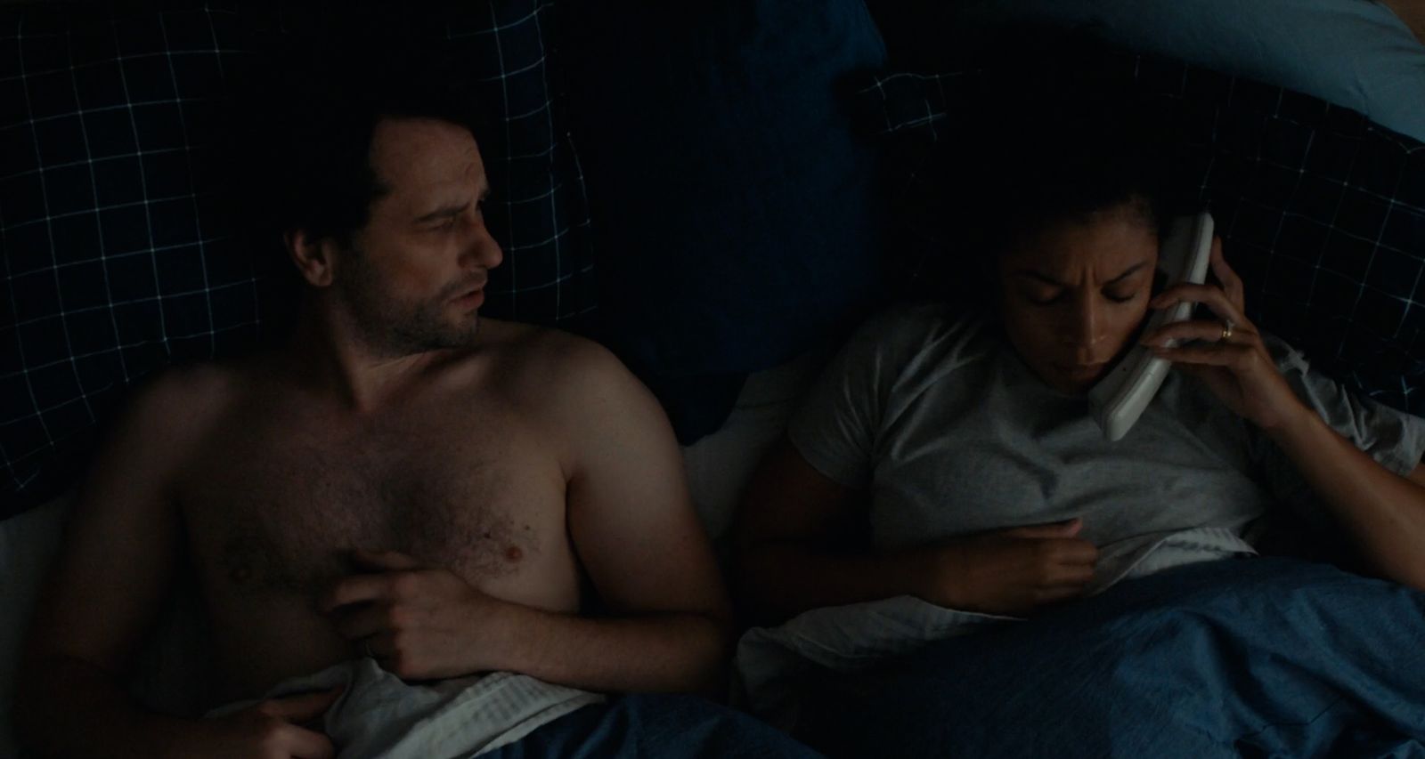 a man and a woman laying in bed talking on cell phones