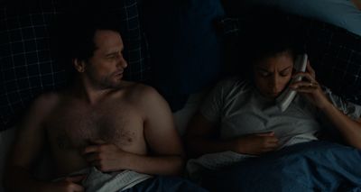 a man and a woman laying in bed talking on cell phones