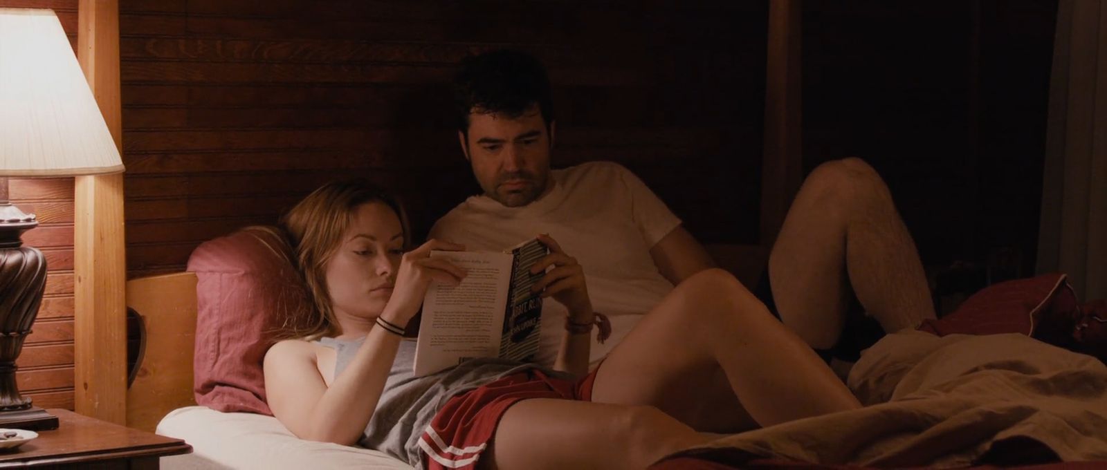 a man and a woman laying in bed reading a book