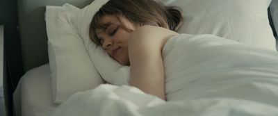 a woman is sleeping in a bed with white sheets