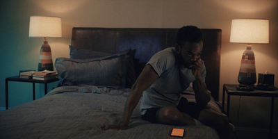 a man sitting on a bed talking on a cell phone