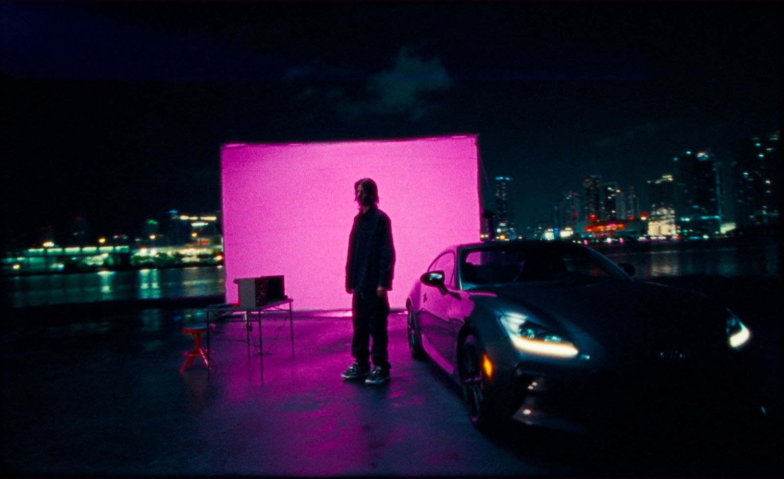 a man standing next to a car in front of a pink screen
