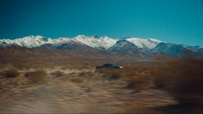 a car driving through the desert with mountains in the background