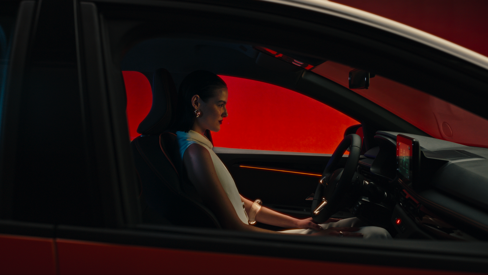 a woman sitting in a car with her hand on the steering wheel