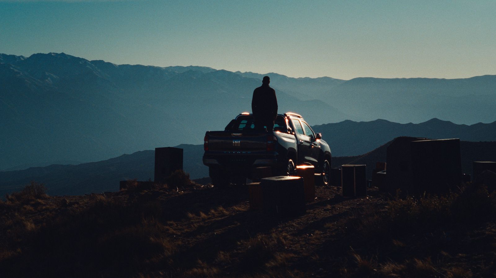 a man standing on top of a truck in the mountains