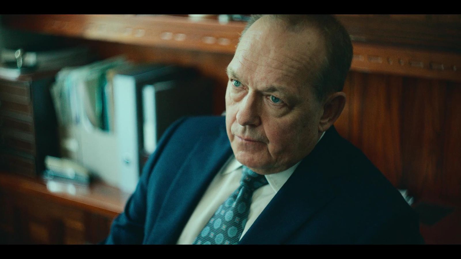 a man in a suit and tie sitting in front of a bookshelf