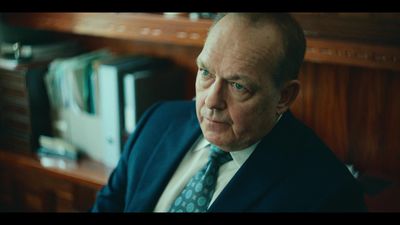 a man in a suit and tie sitting in front of a bookshelf