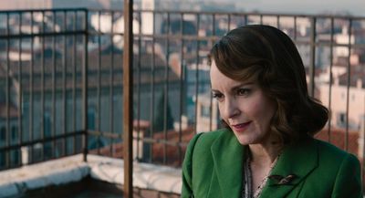 a woman in a green jacket standing on a balcony