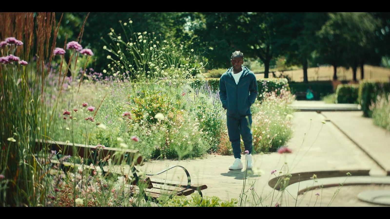 a man walking down a sidewalk next to a lush green field