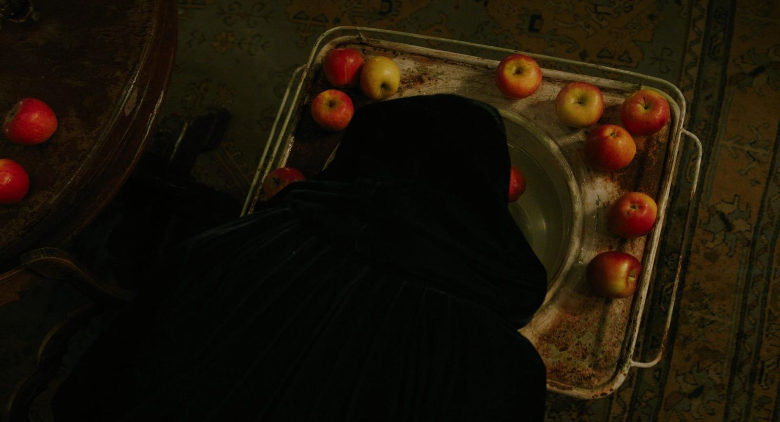 a woman in a black dress standing in front of a tray of apples