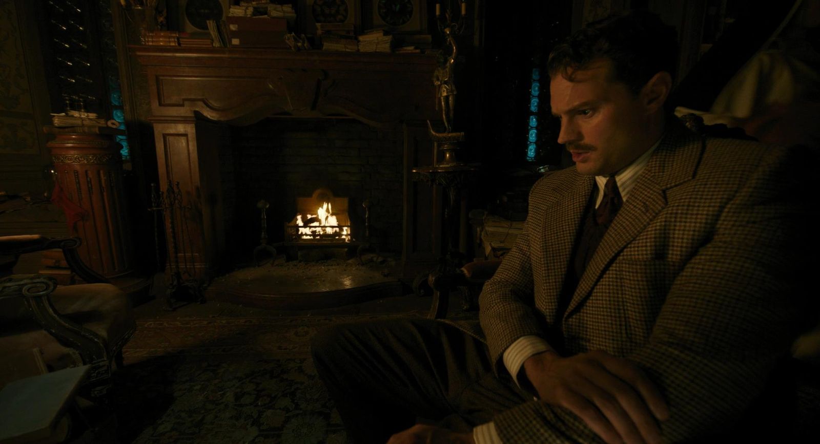 a man in a suit sitting in front of a fire place