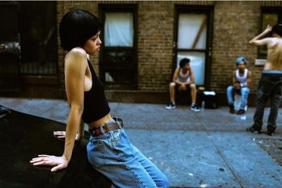 a woman leaning on a car in front of a group of people