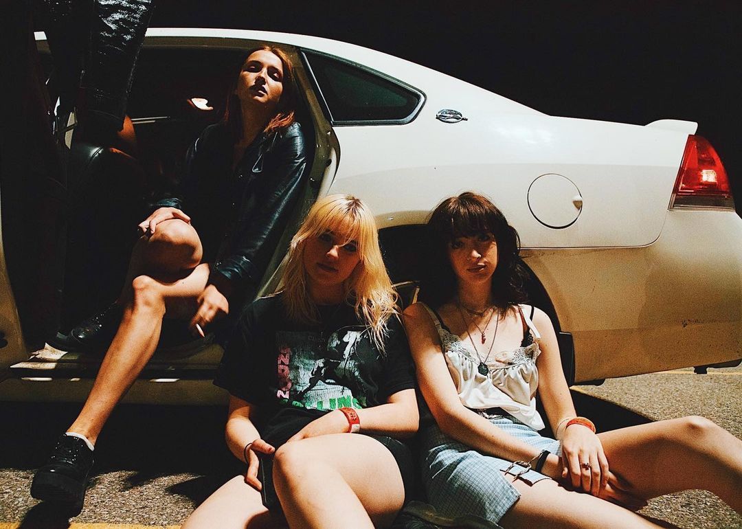 a group of young women sitting next to a white car