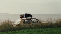 a car with luggage on top of it driving down a road