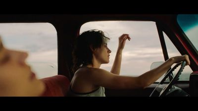 a woman sitting in a car with her hand on the steering wheel