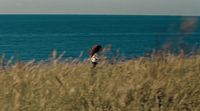 a woman standing on top of a grass covered field next to the ocean