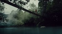 a man walking across a suspension bridge over a river