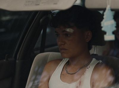 a woman sitting in a car wearing a white tank top