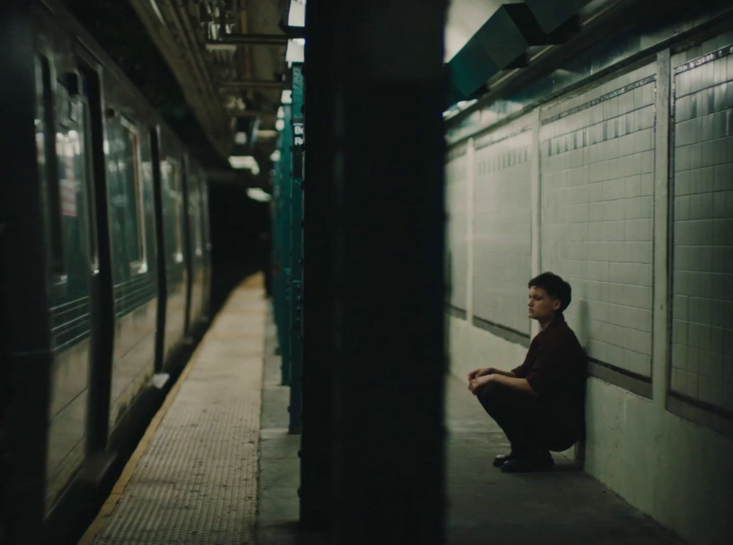 a man sitting on a subway platform next to a train