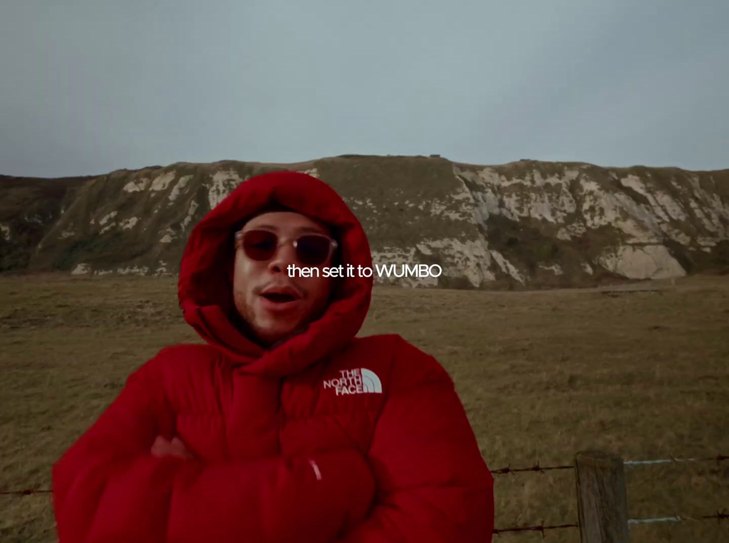 a man in a red jacket is standing in front of a fence