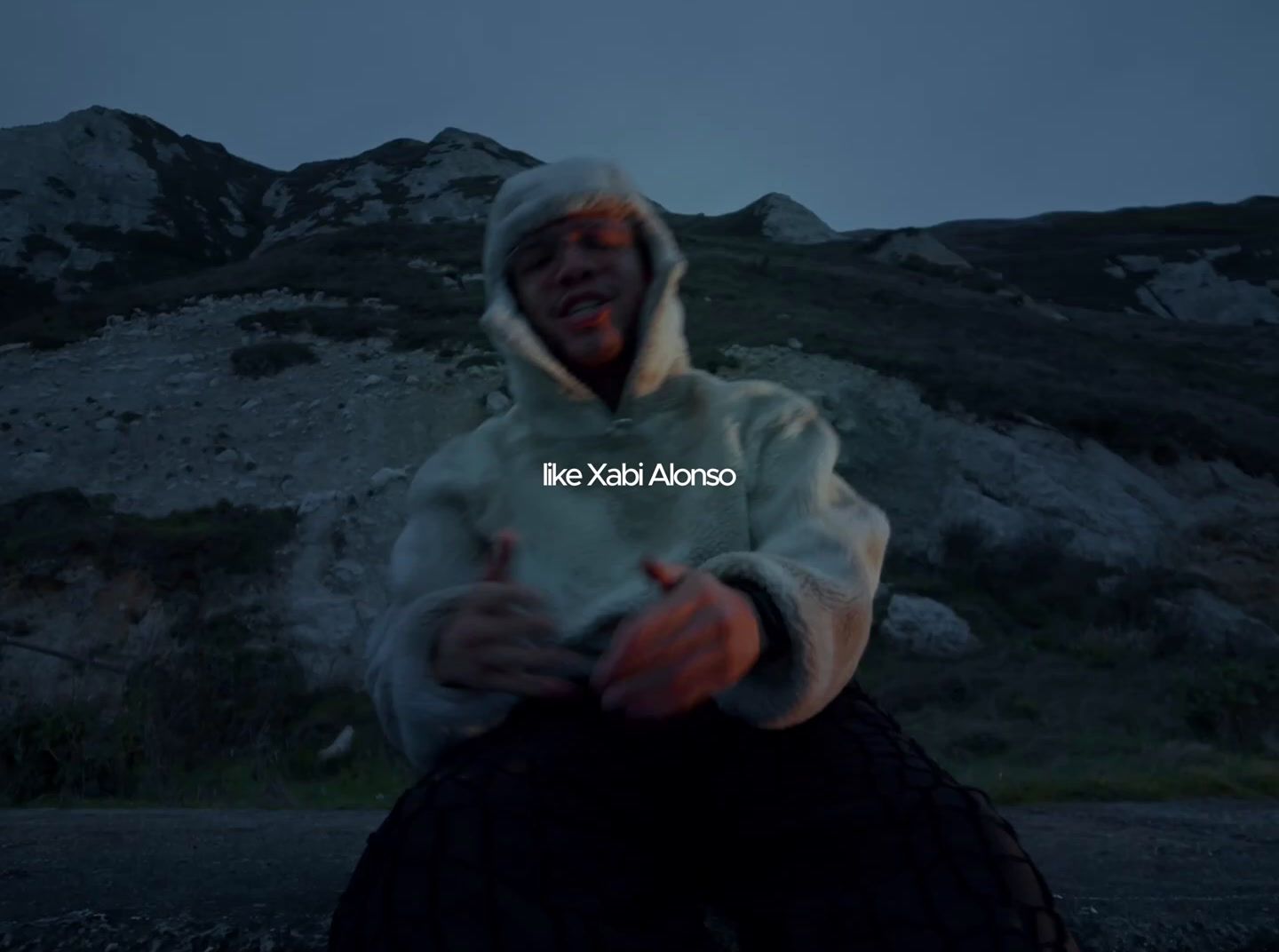 a man in a hoodie sitting on top of a rock